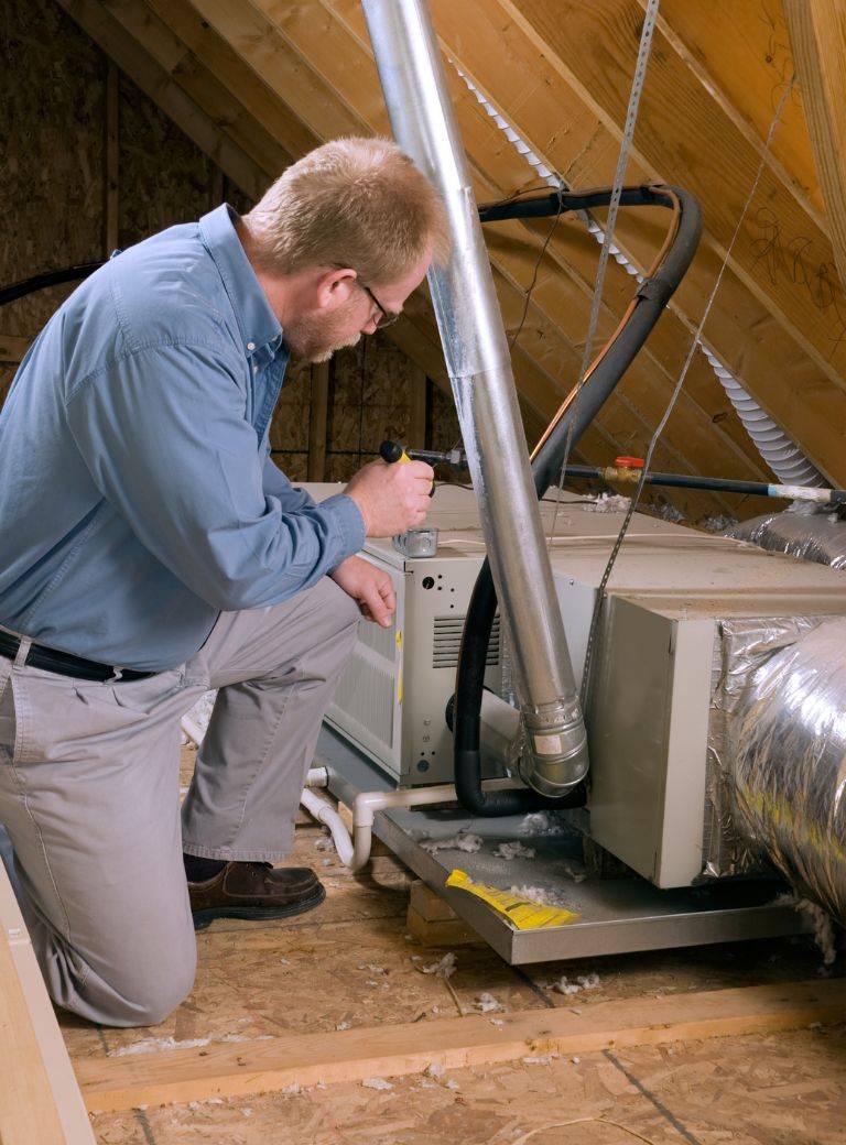 A technician servicing a furnace in an attic